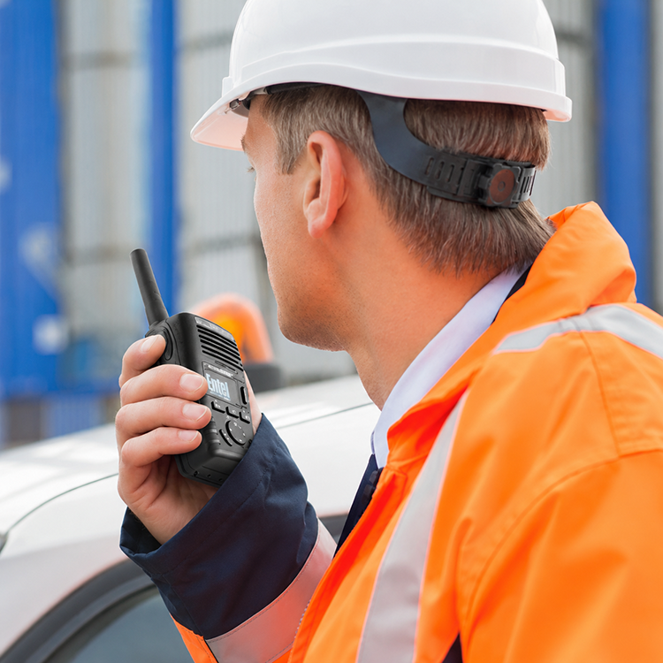 Guy with Entel Radio In Hand- Radio Industries Industrial worker using an Entel handheld two-way radio on-site, wearing high-visibility safety clothing and hard hat in a commercial work environment - available from Radio Industries