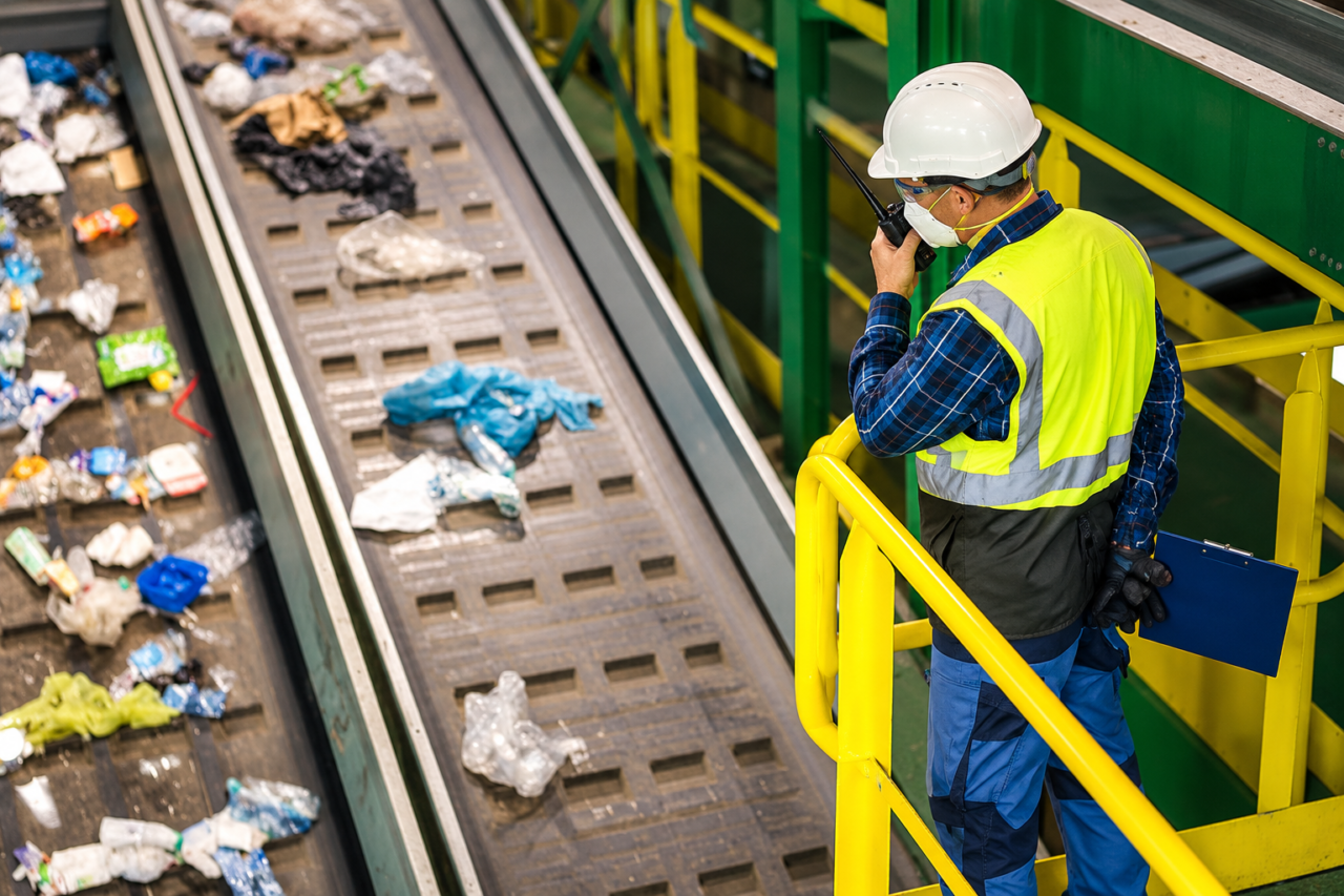 Recycling plant supervisor using waste management two-way radios above a sorting conveyor