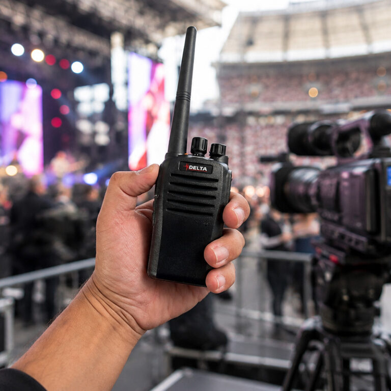 two-way-radio-hire-stadium-event-camera-crew-delta-ds300 | Radio Industries Australia Two way radio hire for stadium events and live productions, featuring a Delta DS300 handheld radio in a camera operator's hand with a professional event and concert background.